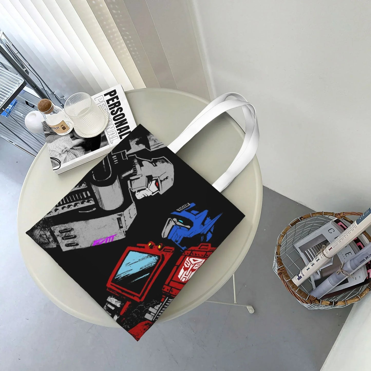 Tote bag noir avec dessins de robots bleus, rouges et gris posés sur une table ronde – Transformers.