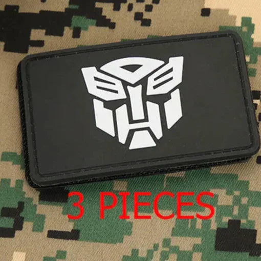 Patch rectangulaire noir avec logo blanc Autobots sur fond camouflage, texte 3 PIECES – Transformers.