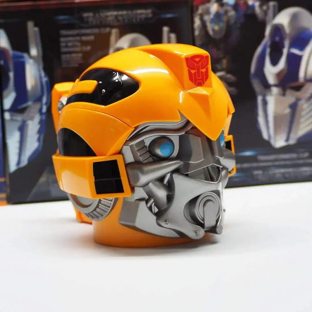 Casque jouet Bumblebee jaune et gris, détails argentés, sur fond de boîtes colorées – Transformers.