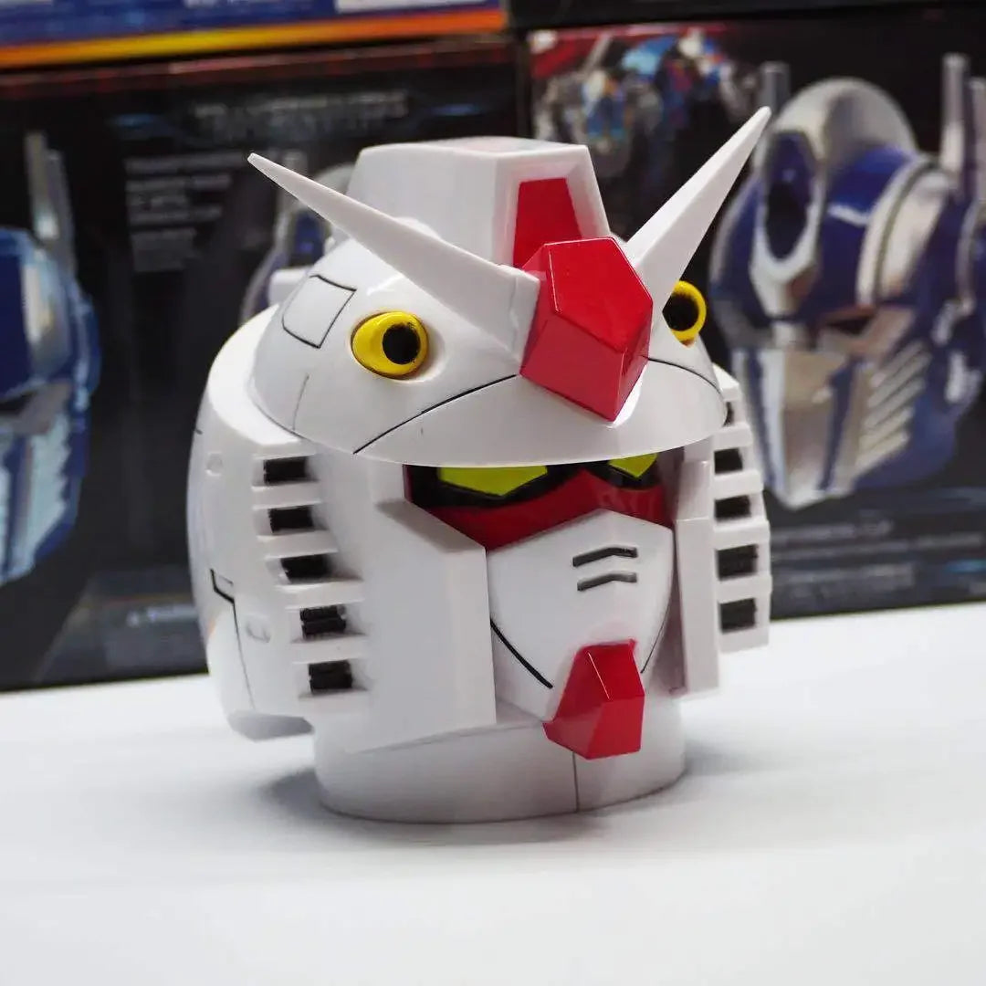 Casque robot blanc et rouge style Gundam, figurine tête détaillée sur fond de boîtes – Transformers.