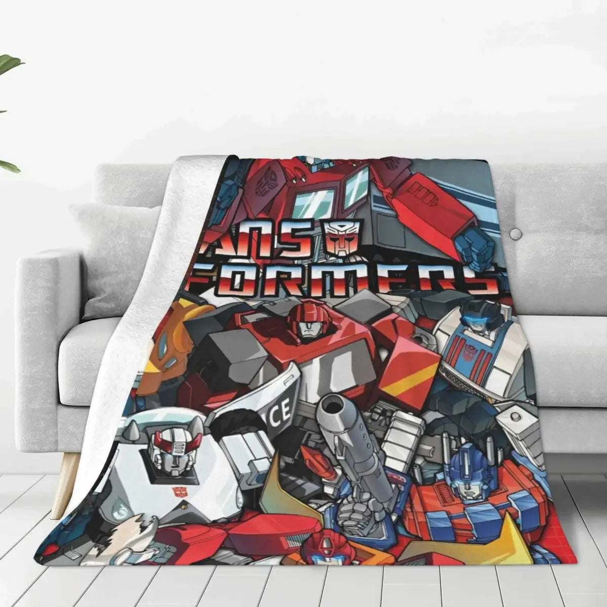 Plaid avec illustration de robots Autobots colorés sur un canapé, logo Transformers visible – Transformers.