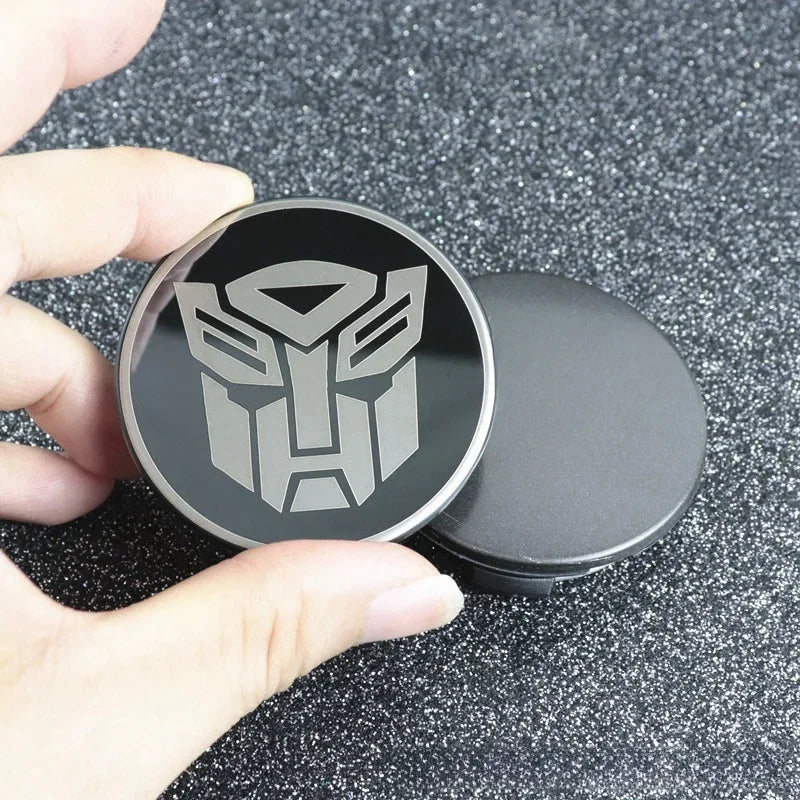 Badge métallique rond logo Autobot argenté sur fond noir, fond pailleté – Transformers.