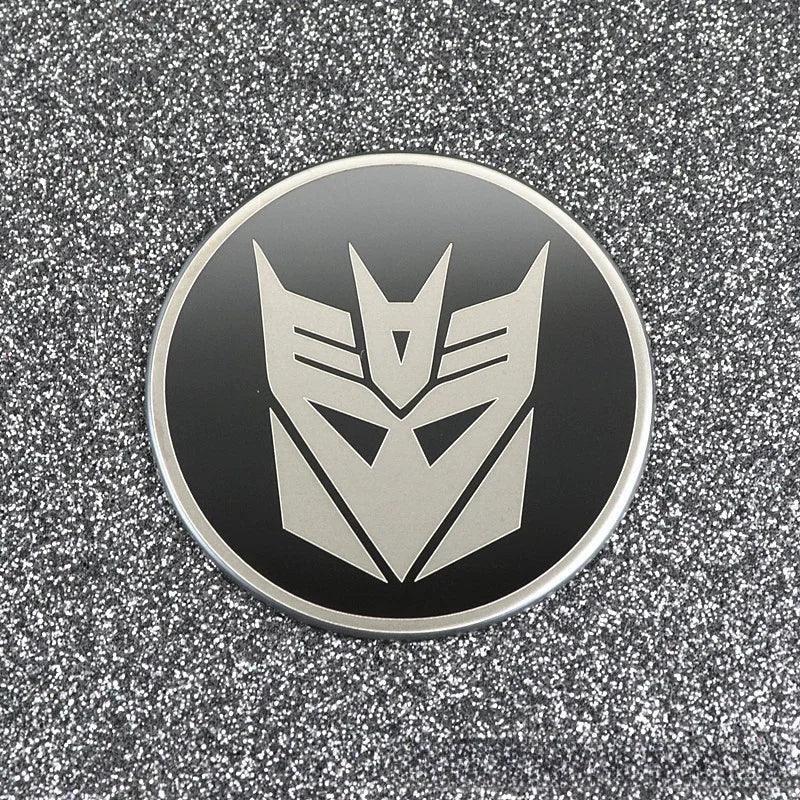 Badge rond noir avec logo Decepticon argenté sur fond pailleté – Transformers.