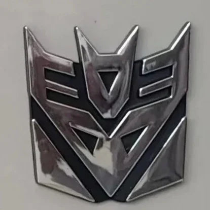 Insigne argenté Decepticon en relief, fond noir, finition métallique, design angulaire – Transformers.