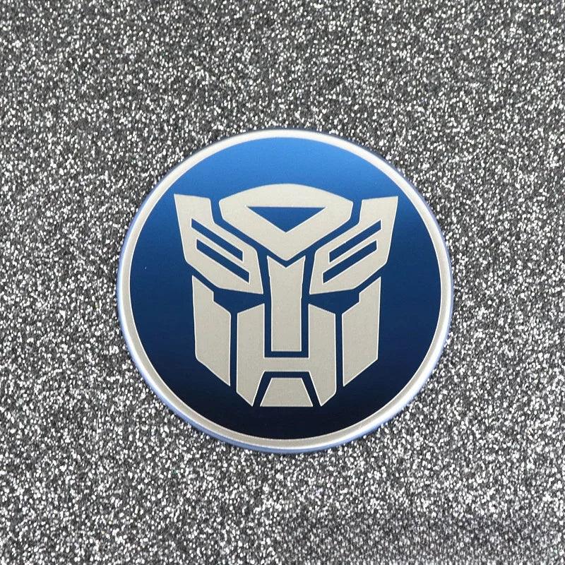 Badge rond bleu avec logo Autobot argenté sur fond pailleté argenté – Transformers.