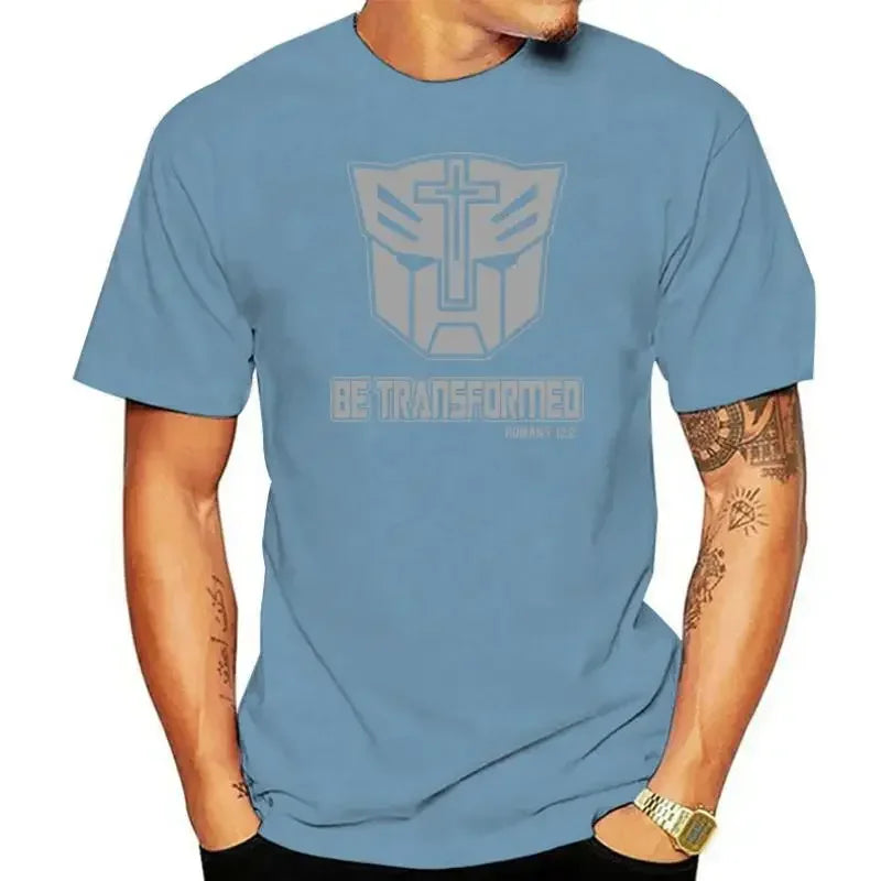 Homme portant un t-shirt bleu avec logo Transformers et croix, texte Be Transformed – Transformers.