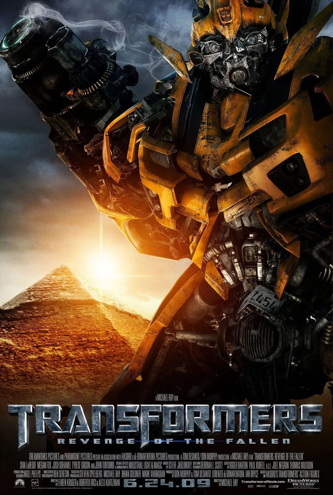 Affiche de film avec robot jaune en gros plan, bras levé, pyramide en arrière-plan au coucher de soleil – Transformers.